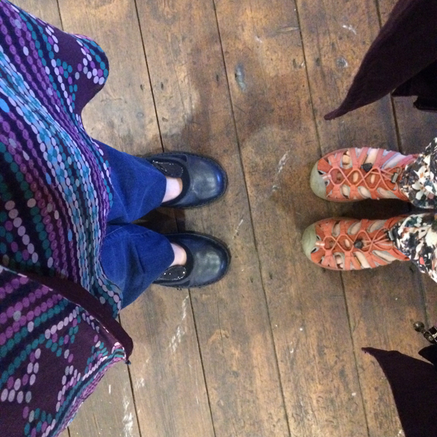 Camera looking down and 2 people facing each other's shoes standing on dark wood floor