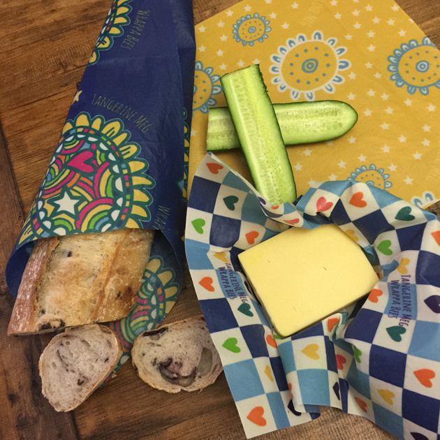 Flay lay shot of cheese, cucumber and a roll, wrapped in Tangerine Meg design Wrappa Bees reusable food wraps