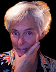 A white-haired lady with her hand on her jaw looks at the camera with a smile